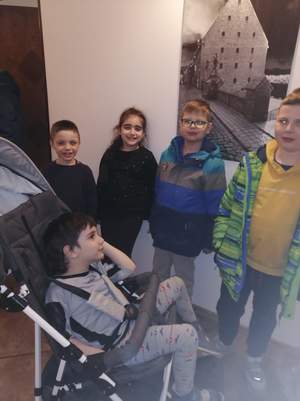 Czworo dzieci stoi pod ścianą , a jedno siedzi na wózku