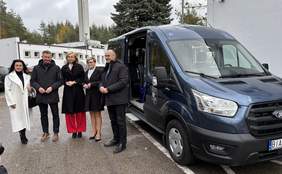 Pokaż zdjęcie: Grupa pięciu osób stoi obok nowego niebieskiego mikrobusa marki Ford Transit, przystosowanego do przewozu osób z niepełnosprawnościami. Samochód ma widoczny symbol wózka inwalidzkiego i oznaczenie Powiatu Białostockiego. W tle znajduje się budynek Domu Pomocy Społecznej w Uhowie.