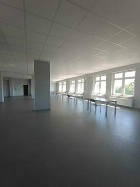 Pokaż zdjęcie: Wyremontowana i zmodernizowana sala z dużymi oknami, na środku stoją stoły z krzesłami.