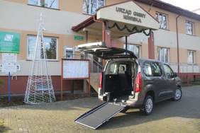 samochów koloru szarego z otwartym tyłem i wysuniętą rampą stoi przed budynkiem urzędu gminy