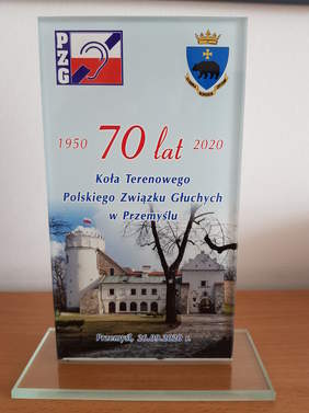 okolicznościowa statuetka, szklana, kształ prostokątny, widok zamku w Przemyślu, lewy górny róg logo PZG, prawy górny herb Przemyśla, napis dotyczący jubileuszu 70 lecia