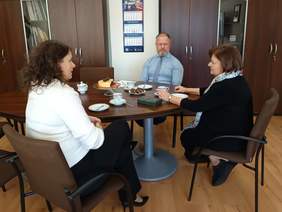 Dwie kobiety i mężczyzna, siedzą przy stole, kobiety patrzą na siebie w trakcie rozmowy