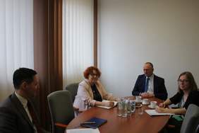 Przy stole w gabinecie siedzą 4 osoby, dwie kobiety, dwóch mężczyzn, rozmawiają, uśmiechają się
