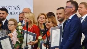 Pokaż zdjęcie: Osoby nagrodzone, kobiety i mężczyźni stoją na scenie. W rękach trzymają róże, dyplomy i statuetki. Wszyscy są uśmiechnięci