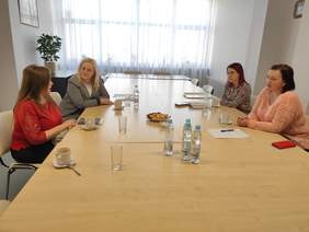 Pokaż zdjęcie: Przy długim stole, w sali konferencyjnej stole siedzą cztery kobiety i rozmawiają. 