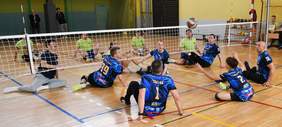 Pokaż zdjęcie: Osoby z niepełnosprawnościami grają w siatkówkę na siedziąco i są ubrani na sportowo