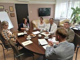 Uczestnicy spotkania siedzą przy owalnym stole  - w sumie 6 osób
