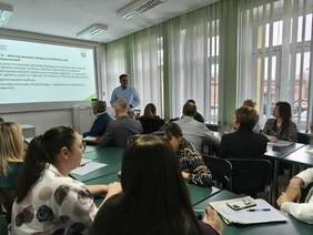 Pokaż zdjęcie: Trwa spotkanie na temat „Programu wyrównywania różnic między regionami III”. Przy stolikach siedzą ludzie i patrzą na prezentację wyświetloną na tablicy multimedialnej. Obok stoi prowadzący spotkanie. 