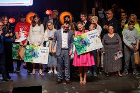 Pokaż zdjęcie: Finał Festiwalu - na scenie stoją Laureaci, jurorzy oraz prowadzący. Laureaci trzymają nagrody - duże symboliczne czeki. 