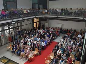 Pokaż zdjęcie: fotografia wykonana z balkonu, widok na całe atrium, sala wypełniona gośćmi spotkania. 