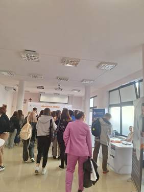 Pokaż zdjęcie: Korytarz na uczelni, po obu stronach korytarza poustawiano stoiska informacyjne, pomiędzy chodzą studenci, uczestnicy wydarzenia.