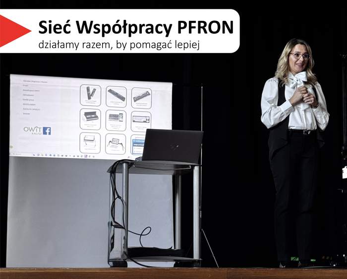 Pokaż zdjęcie: Scena konferencyjna z czarnym tłem i banerem „Sieć Współpracy PFRON”. Pod banerem widać ekran z prezentacją. Na prezentacji obrazy technologii asystujących i wspomagających dla osób z niepełnosprawnościami. Na środku zdjęcia ustawiony jest pulpit z otwartym laptopem. Po prawej stronie stoi kobieta o jasnej karnacji, w okularach, z długimi blond włosami, ubrana w białą koszulę i czarne spodnie. Trzyma w rękach mikrofon i jest skierowana w stronę publiczności. W górnej lewej części zdjęcia widoczny jest napis: „Sieć Współpracy PFRON” oraz mniejszy: „działamy razem, by pomagać lepiej”.