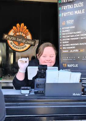 Pokaż zdjęcie: Kobieta z zespołem Downa macha przez okienko food truck`a