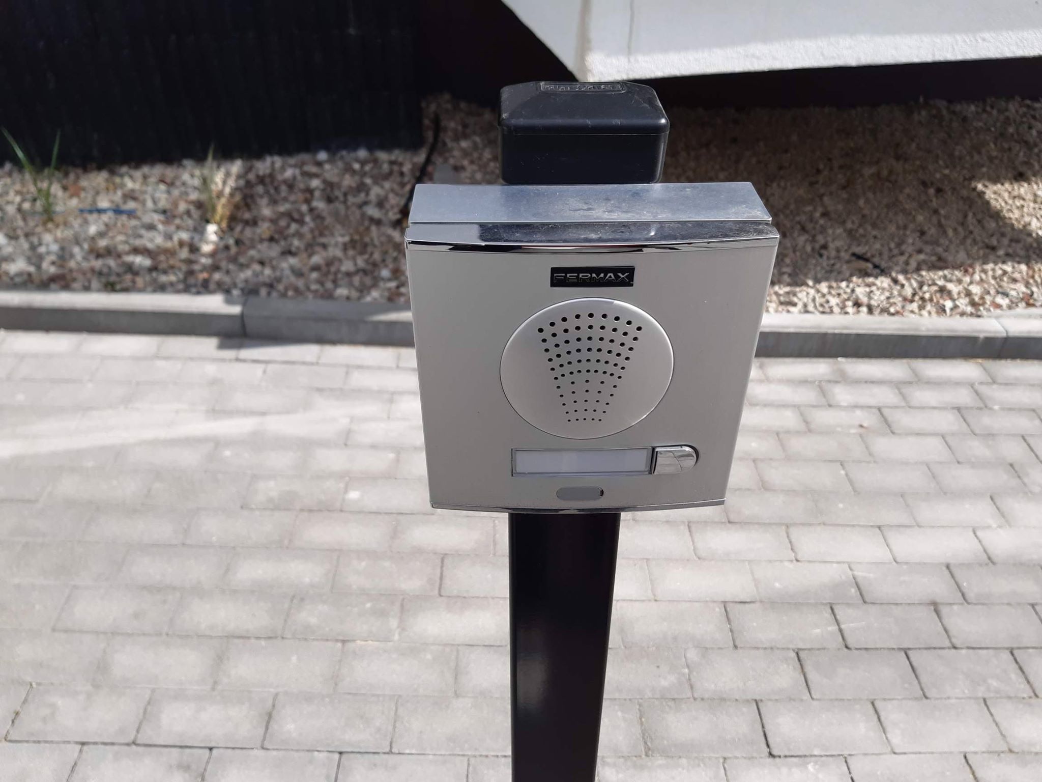 Urządzenie komunikacyjne przy wjeździe na parking. Urządzenie techniczne służące do wzywania obsługi bądź pomocy na czarnym słupku na tle chodnika z kostki betonowej