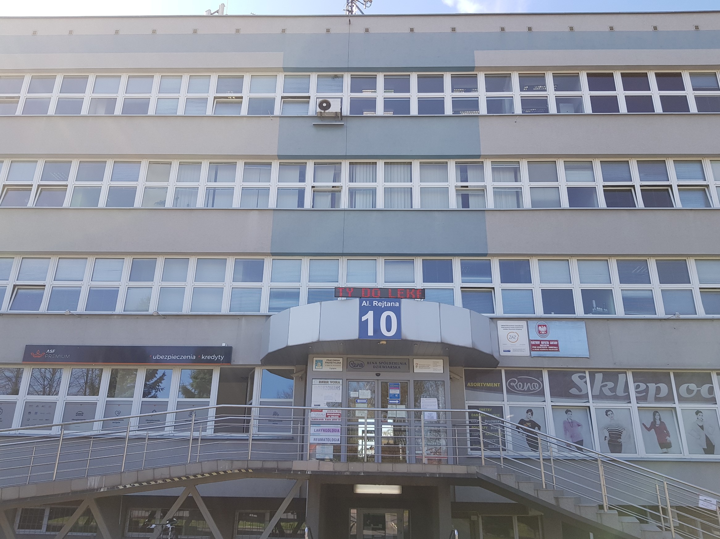 Wejście główne do siedziby Oddziału Podkarpackiego PFRON Szary, czterokondygnacyjny budynek, o mocno przeszklonej elewacji. W centralnym punkcie wyniesione nad poziom gruntu wejście do budynku. Po prawej stornie schody, a po lewej pochylnia dla wózków. Na podeście, dom którego prowadzą schody i pochylnia wiatrołap, and którym widać nazwę ulicy i numer budynku.