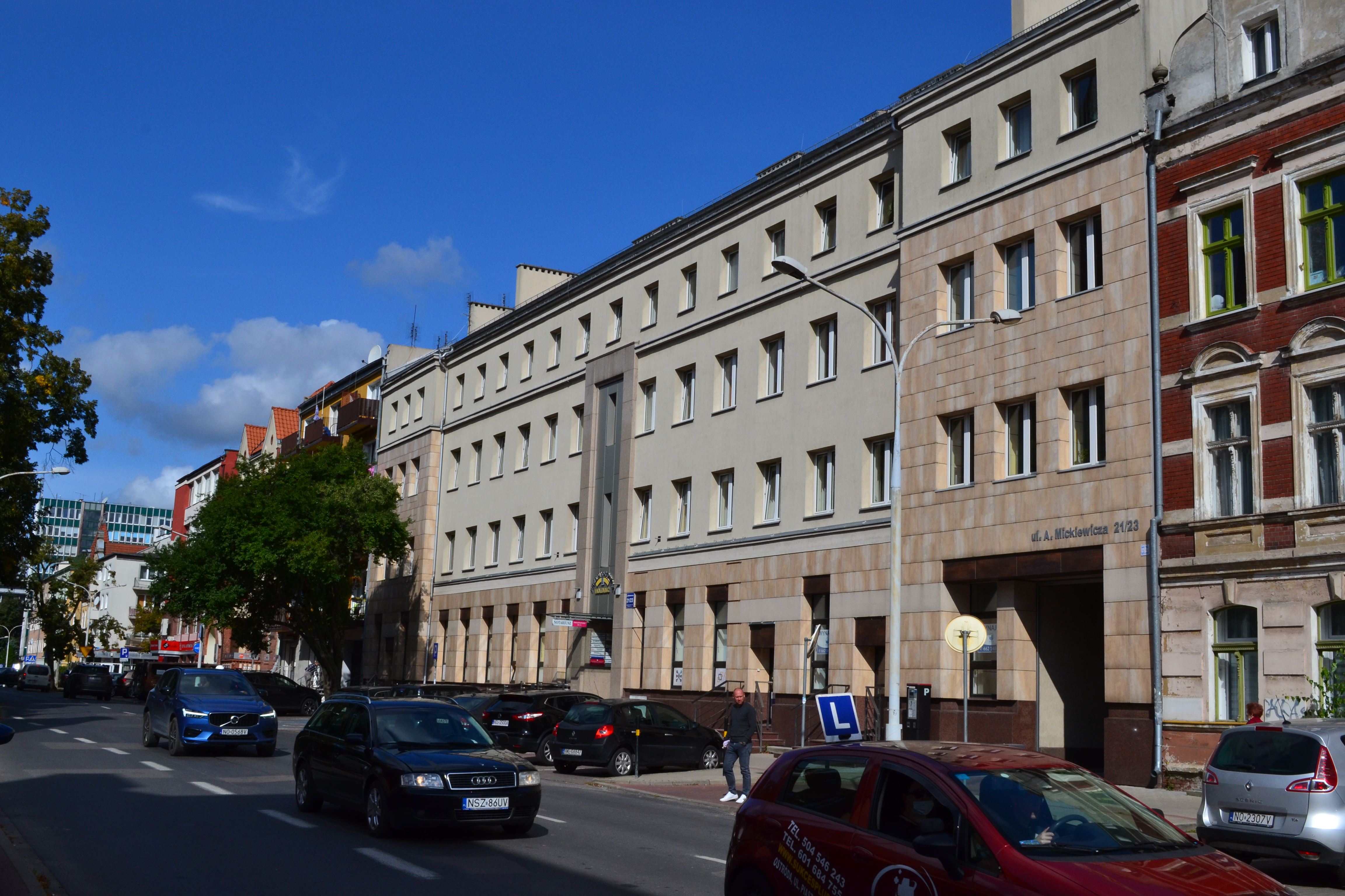 Ulica, na której odbywa się normalny ruch samochodowy. W tle budynek biurowy, obłożony kamieniem. Po prawej stronie wjazd na dziedziniec budynku.