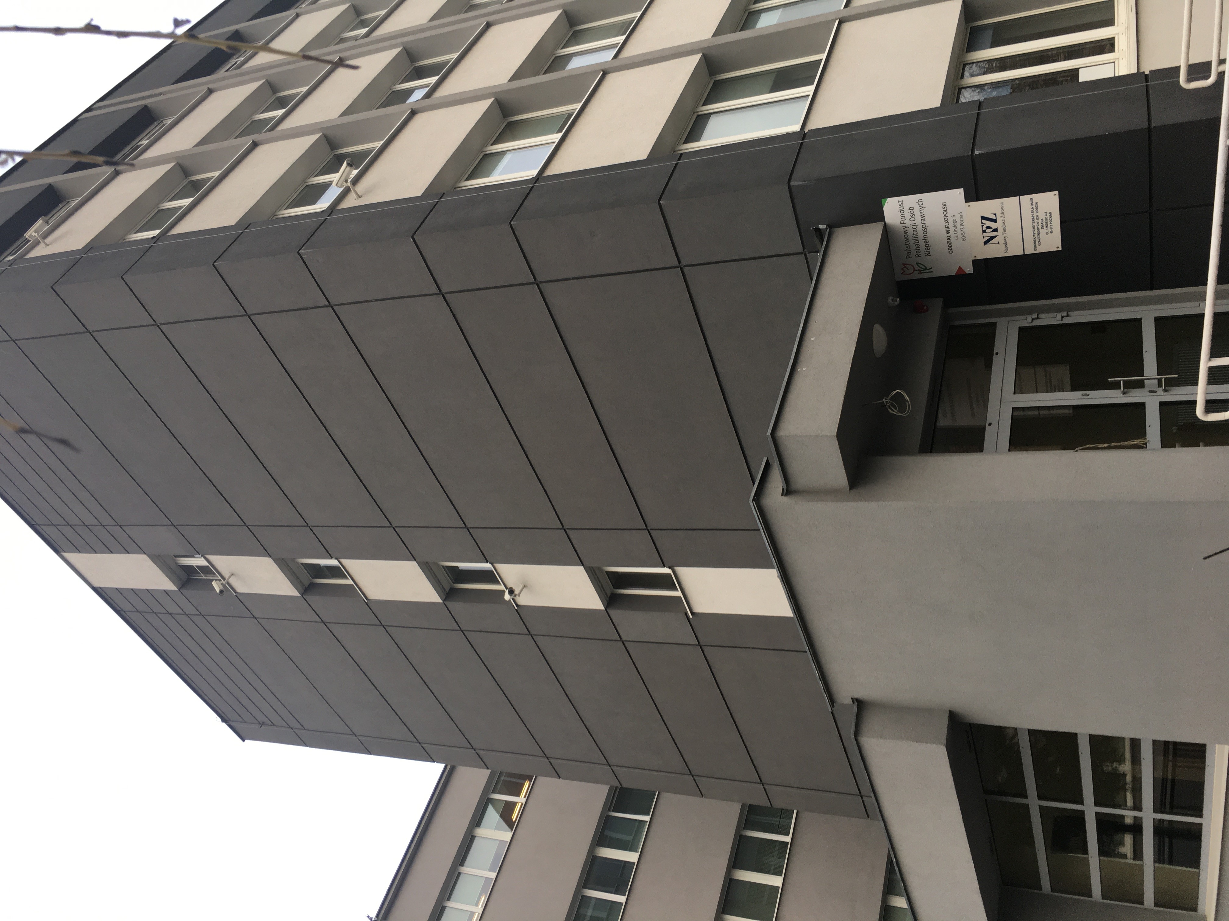Budynek przy ul. Lindego 6 - wejście główne - siedziba Oddziału Wielkopolskiego PFRON Na pierwszym planie szara, parterowa przybudówka, do której prowadzi pochylnia z dwoma poręczami. Po prawej stronie widoczne logo PFRON. Na drugim planie – duży, sześciokondygnacyjny budynek w ciemnoszarym kolorze. Na bocznej ścianie jasny pas pośrodku elewacji. W tle widać jeszcze po lewej stronie szary budynek podobnej wysokości.