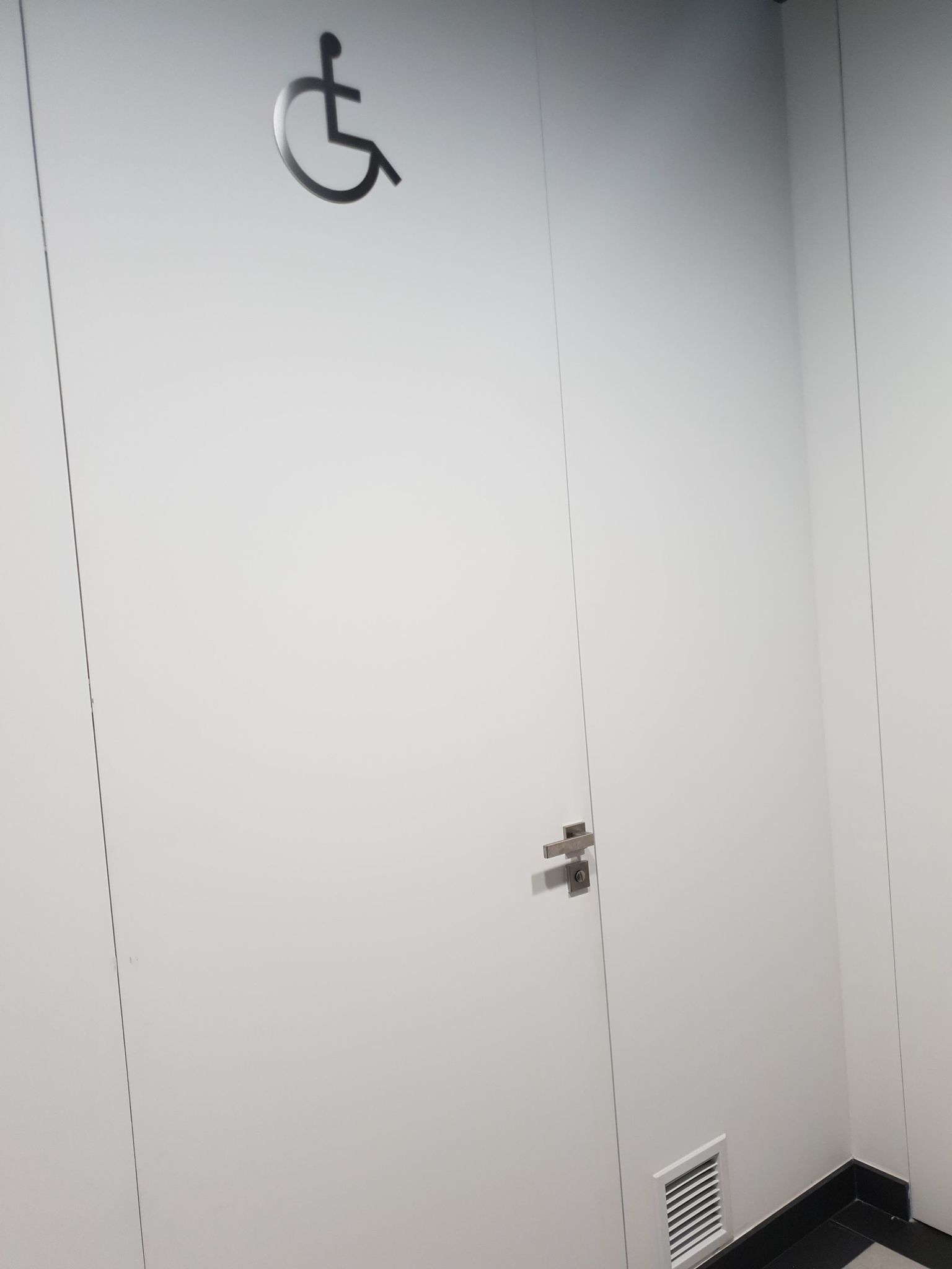 Drzwi do toalety dla osób niepełnosprawnych Drzwi wejściowe do toalety dla niepełnosprawnych koloru białego z dużym piktogramem osoby niepełnosprawnej.