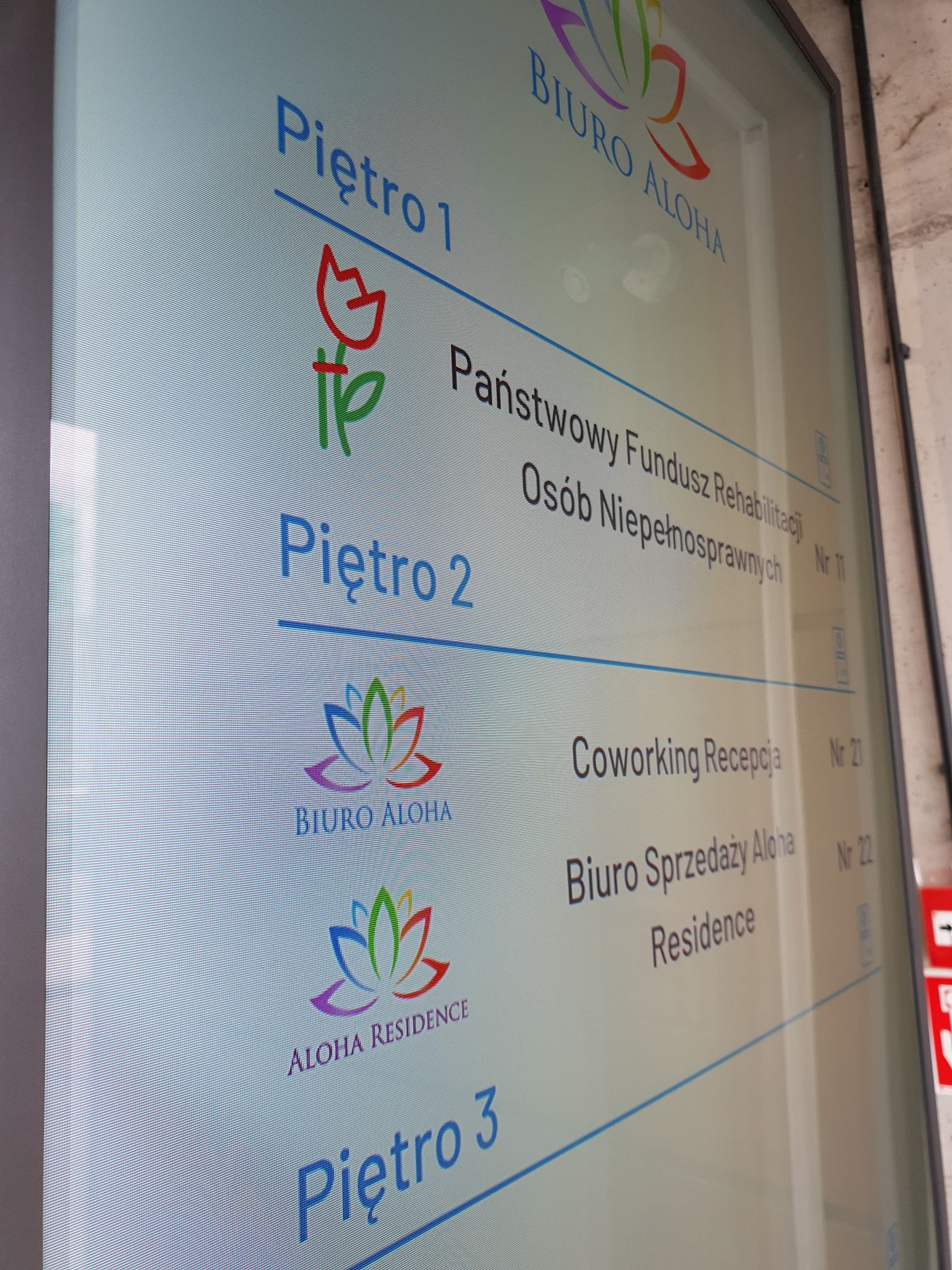 Tablica informacyjna Tablica informacyjna, mówiąca o umieszczonych w budynku instytucjach. Na piętrze pierwszym Państwowy Fundusz Rehabilitacji Osób Niepełnosprawnych. Na piętrze 2 recepcja i biuro sprzedaży