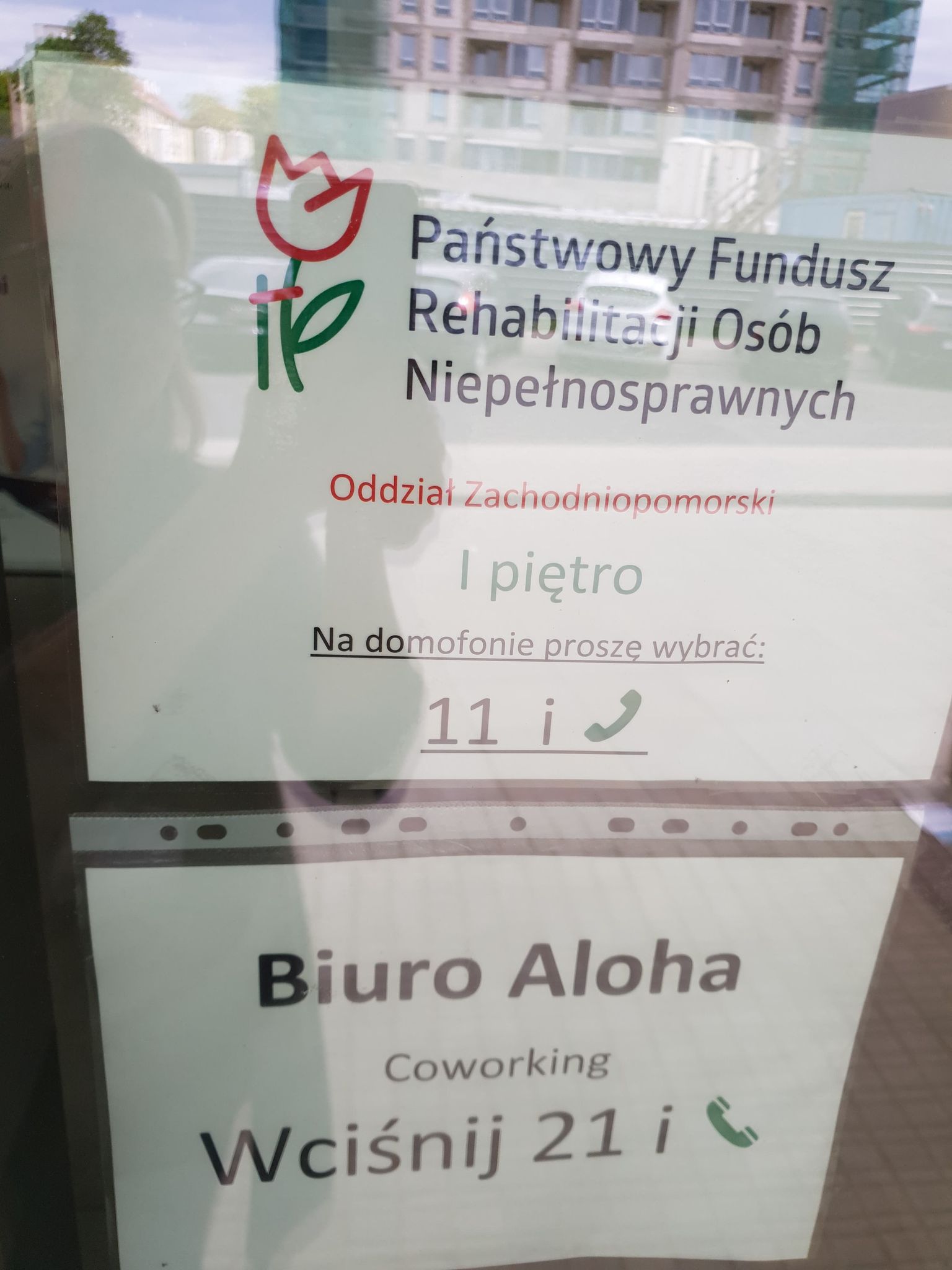Informacje o lokalizacji instytucji Widok tabliczek informacyjnych na drzwiach wejściowych do budynku. Tabliczki zawierają następujące informację: nazwę instytucji, piętro, na którym się znajdują oraz instrukcje obsługi domofonu